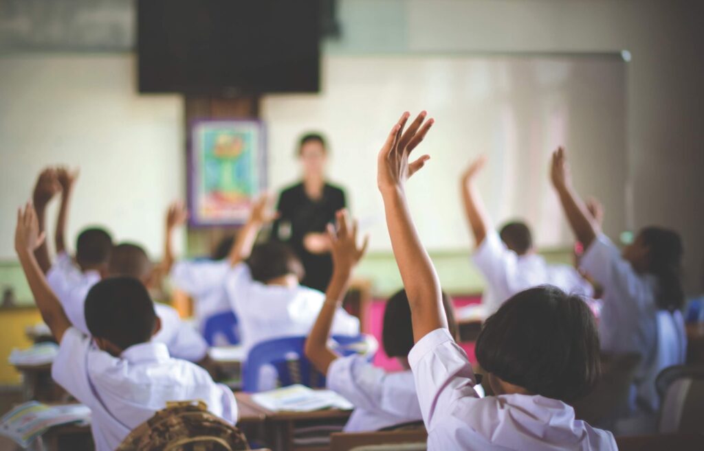 Students raising their hands in a classroom while attending a lesson, representing active learning and the importance of education.