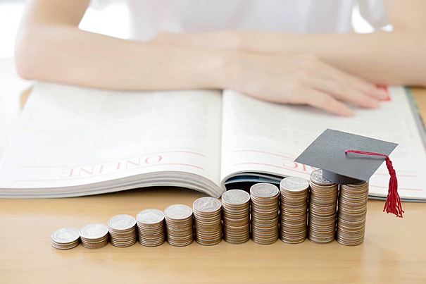 Stacks of coins with a graduation cap placed on top beside an open book, symbolizing investment in education and future success.